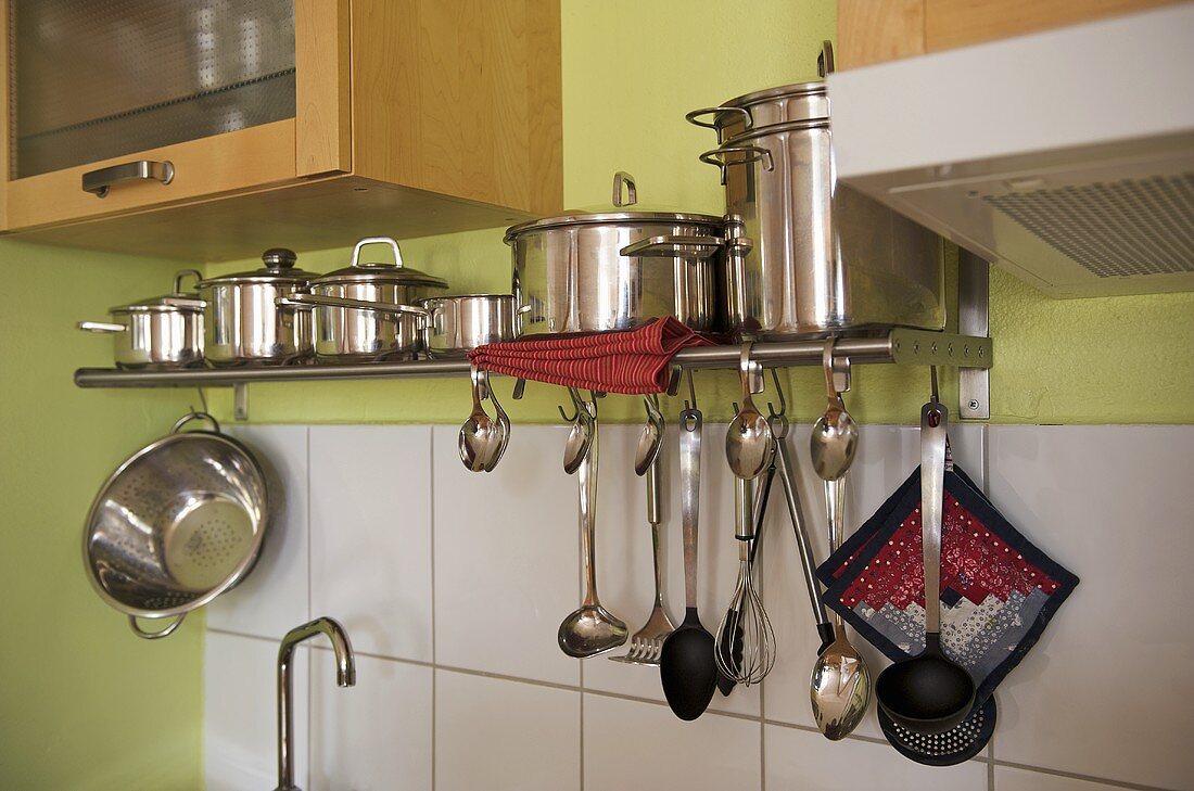 Edelstahltöpfe auf Regal aus Metall und hängende Küchenutensilien