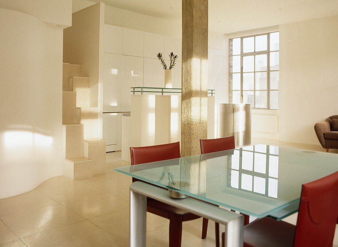 Esstisch mit Glasplatte und roten gepolsterten Stühlen in offener Küche