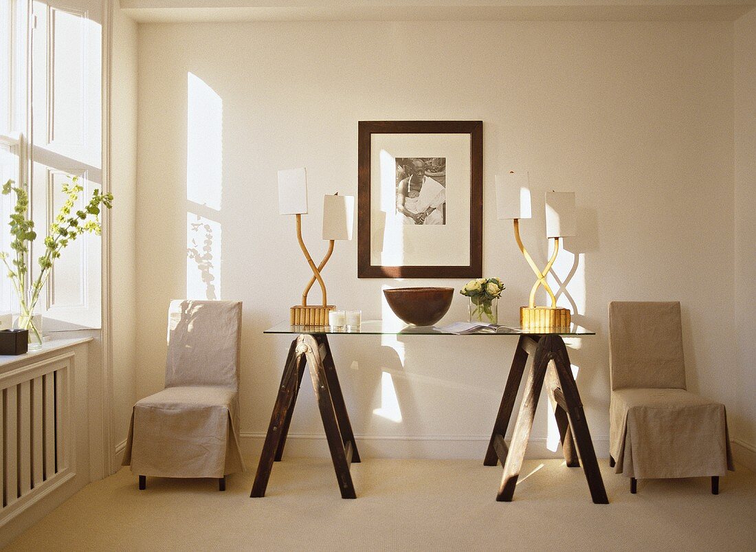 Glasplatte auf Holztischböcken mit Tischlampen und Stühle mit Hussen