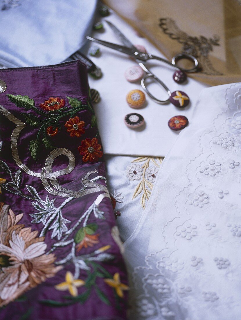 A detail of embroidered fabrics, buttons, scissors,