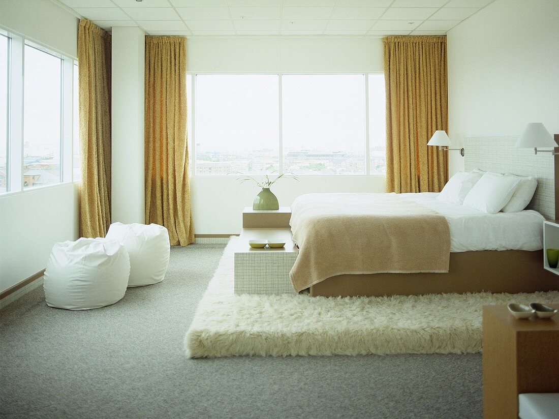 Doppelbett auf Podest mit Flokati belegt und Fensterfront mit gelbem Vorhang