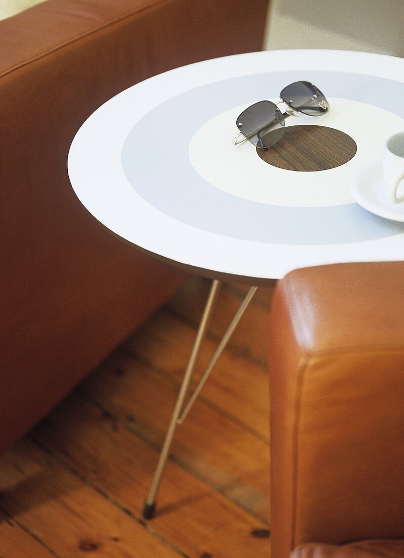 A detail of a modern sitting room, a round painted table, set between leather armchairs, wooden floor,