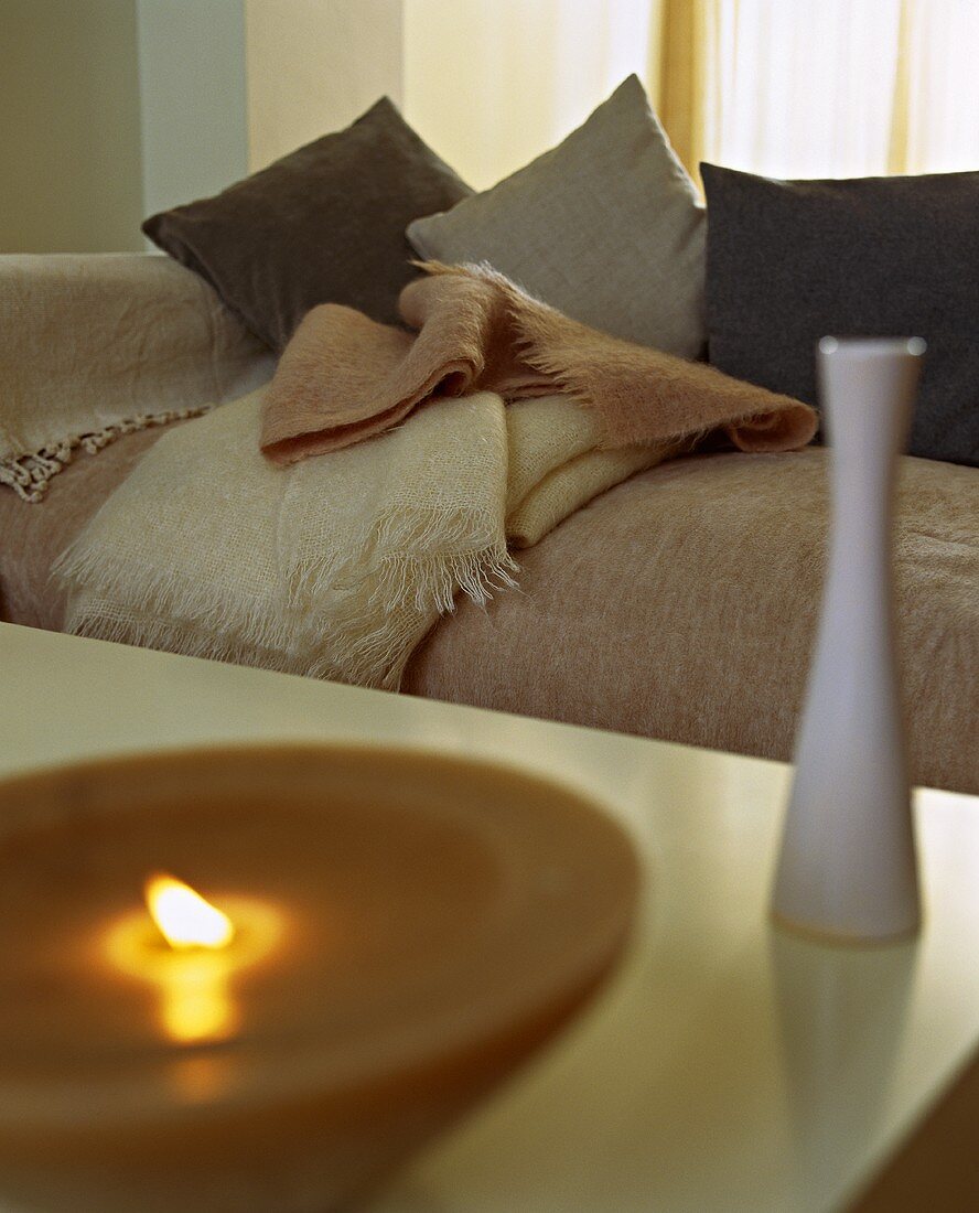 Vase und brennende Kerze auf Tisch vor Couch mit Kissen