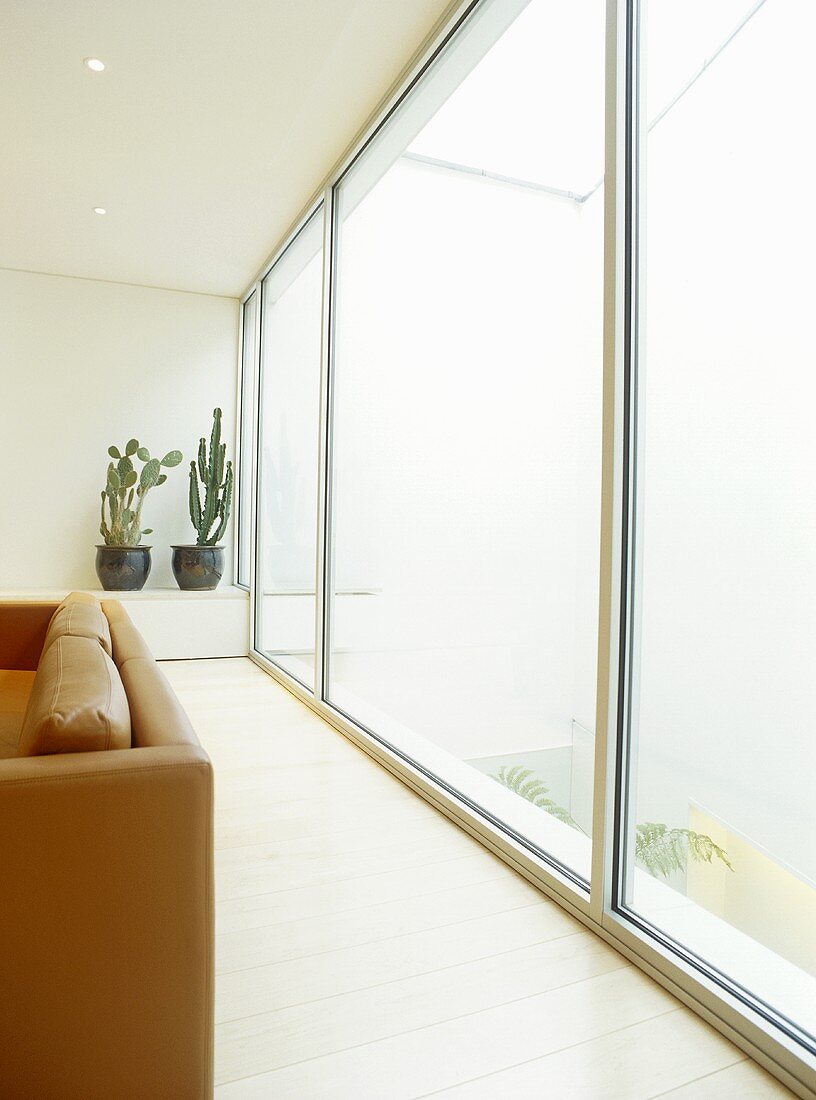 Wohnzimmer mit Rückenlehne einer Ledercouch vor Terrassenfensterschiebetüren