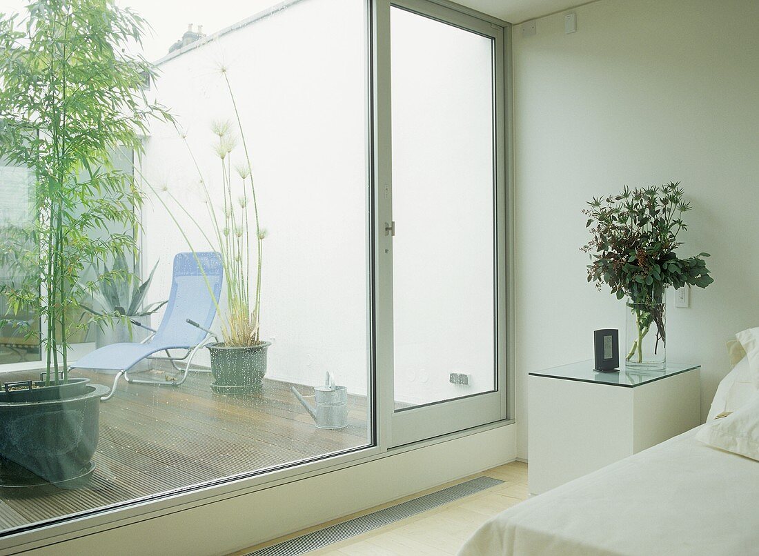 Schlafzimmer mit kubischem Nachttisch vor Fensterfront mit Blick auf die Terrasse