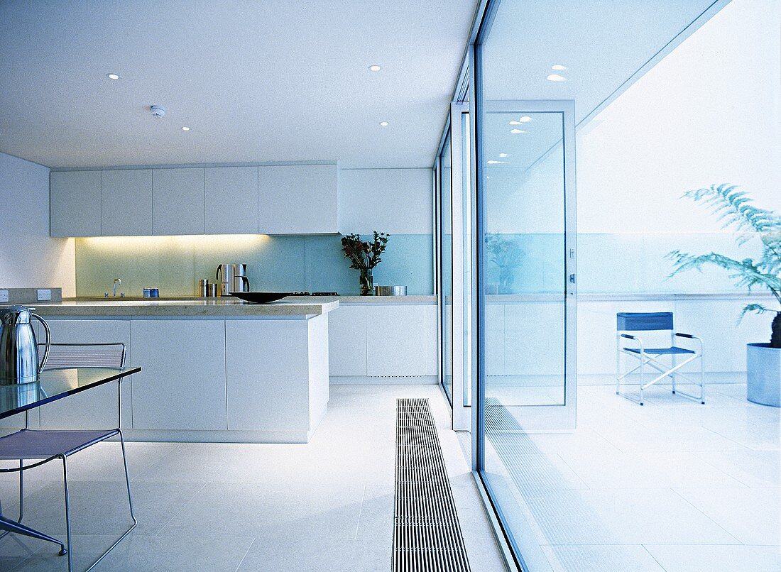 Modern kitchen and dining area with white cabinets, glass backsplash, wall of windows, and a tiled floor.