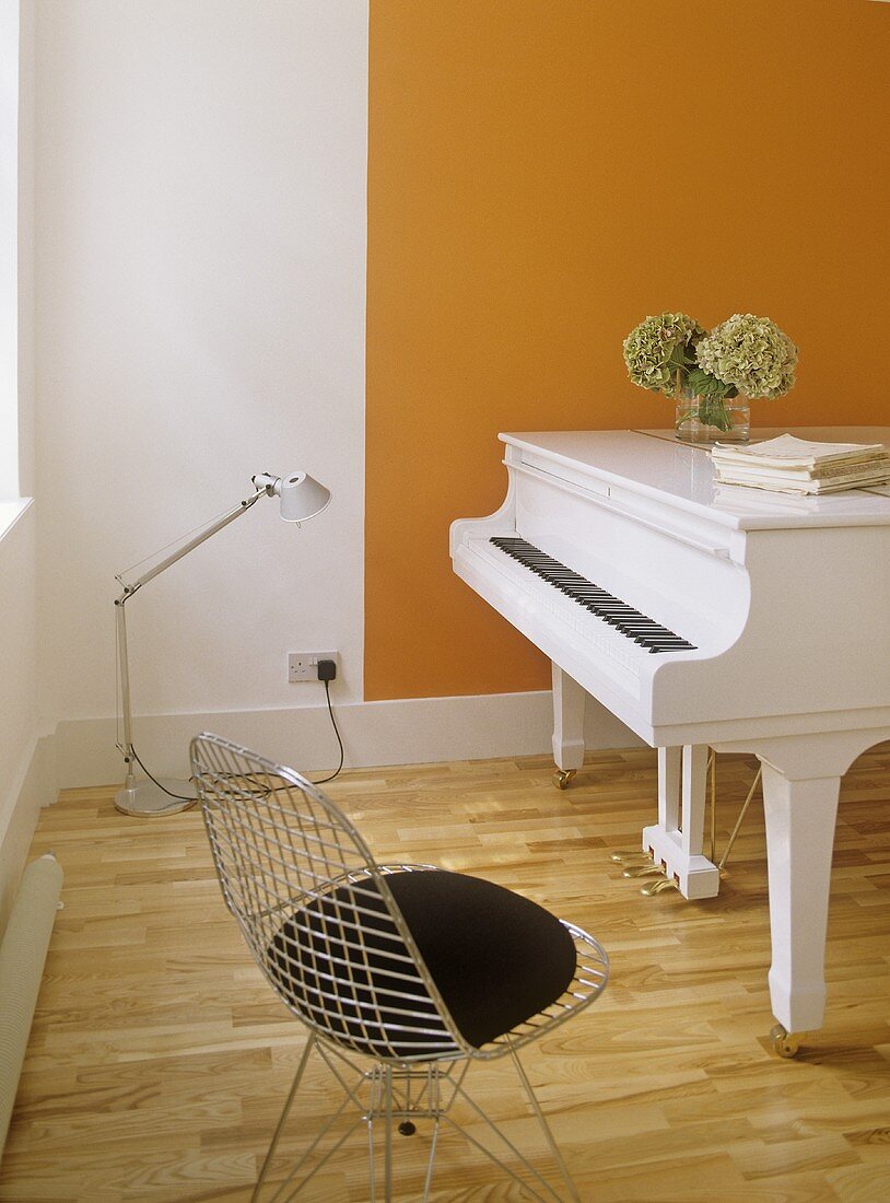 A modern, white and orange minimalist music room, grand piano, metal lattice chair, white and orange walls, hydrangeas in a vase on top of piano,