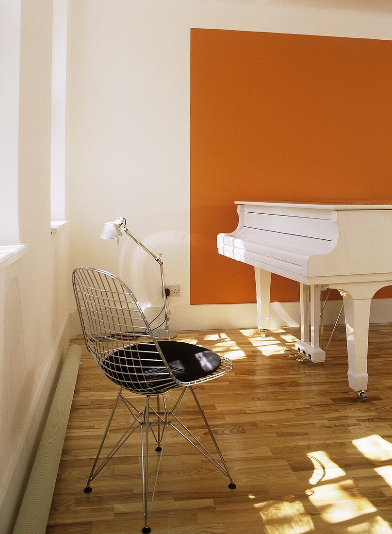 A modern white and orange minimalist music room, grand piano, metal lattice chair, wooden floor, lamp,