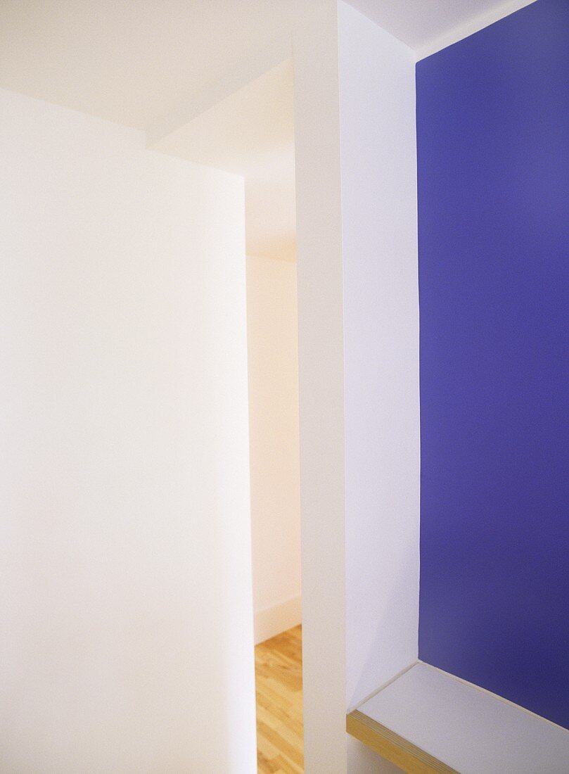 An abstract detail of white and purple walls and a view through a narrow opening into a hallway