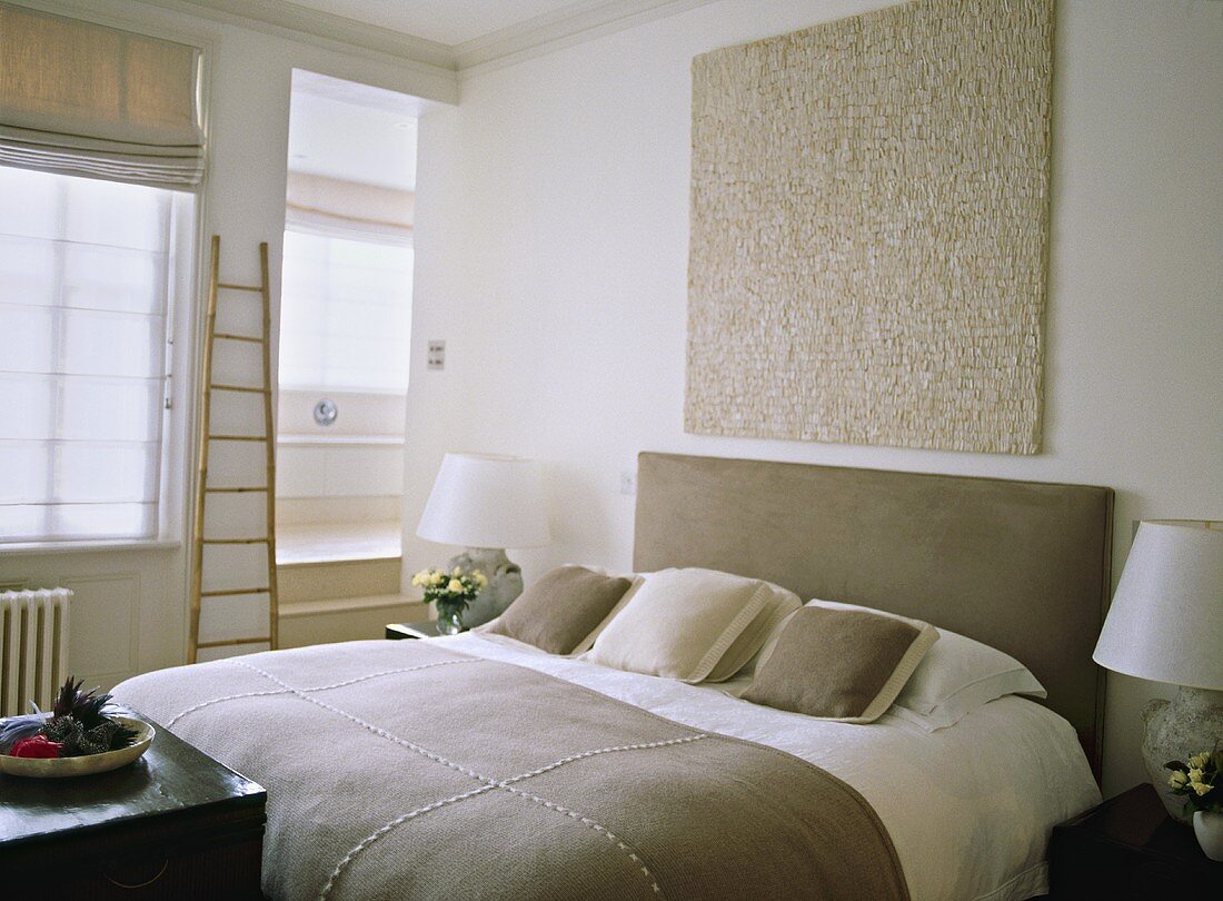 A modern neutral bedroom, double bed with upholstered headboard, side cabinets, textured artwork
