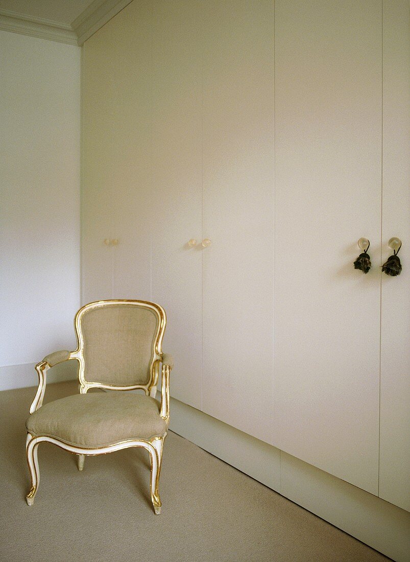 A detail of a bedroom, with a Louis XV style armchair and modern fitted wardrobes