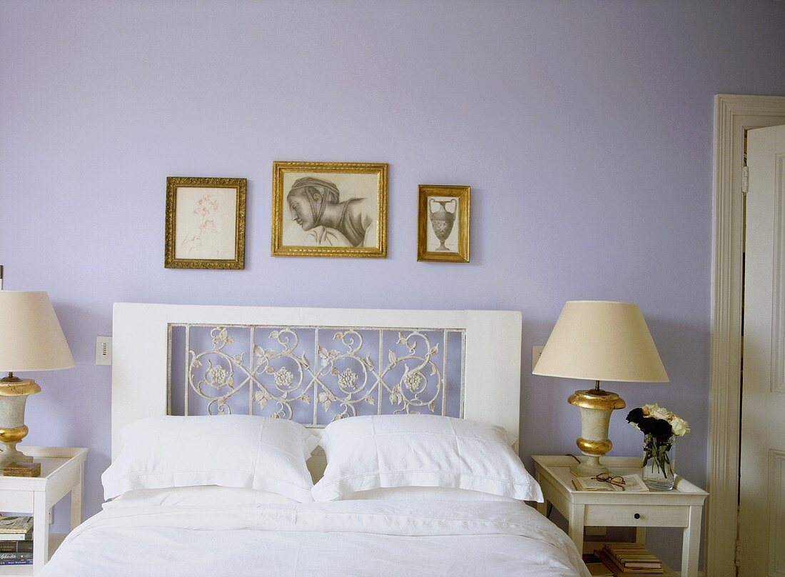 A detail of a traditional, pale blue bedroom with double bed, decorative headboard, side tables, lamps