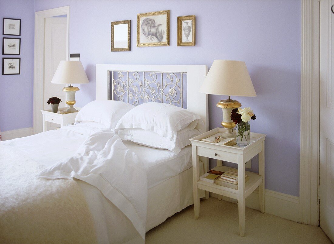 Weisses Doppelbett mit dekorativem Kopfteil und Nachttisch mit Lampen vor blauer Wand