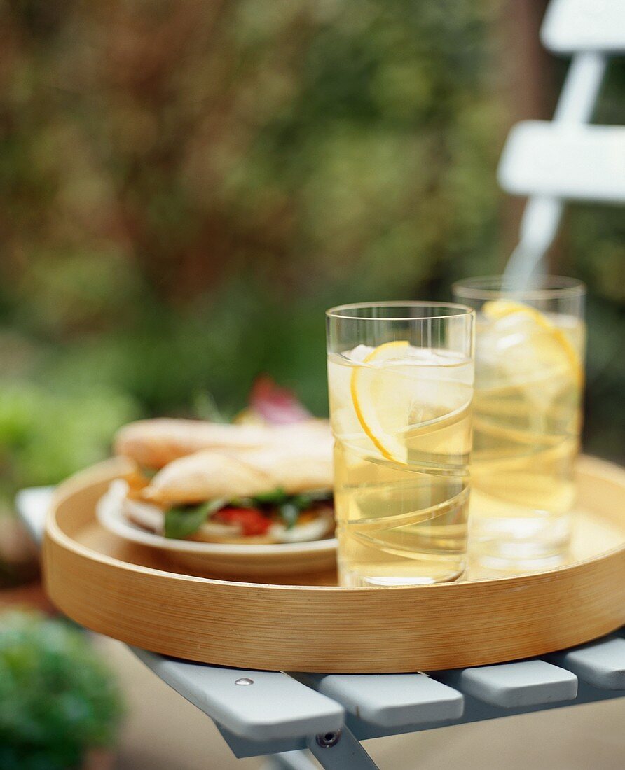 Tablett mit Eistee und Sandwiches auf Gartenstuhl im Freien