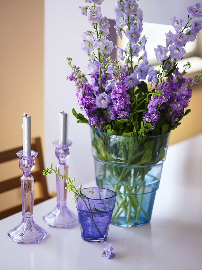 Blaue Glasvase mit lila und rosa Sommerblumen und zwei Kerzen