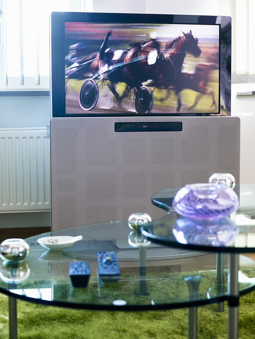 A flat screen television behind a glass coffee table