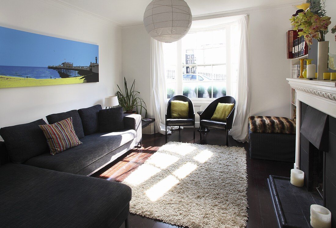 Wohnzimmer mit schwarzen Sitzmöbeln, einem beigefarbenen Flokatiteppich und einem Kamin