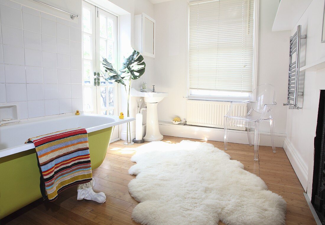 A sheepskin rug in front a green, free-standing bathtub
