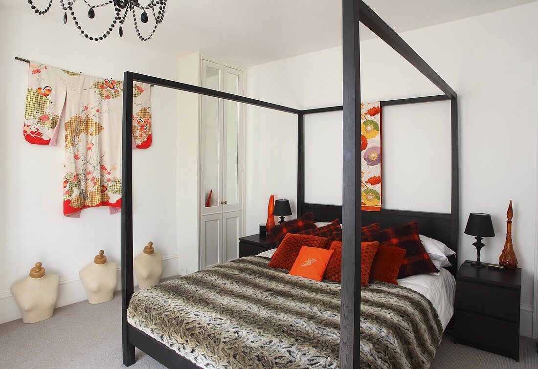 Ein Himmelbett mit Dekokissen und Tagesdecke und ein Kimono an der Wand im Schlafzimmer