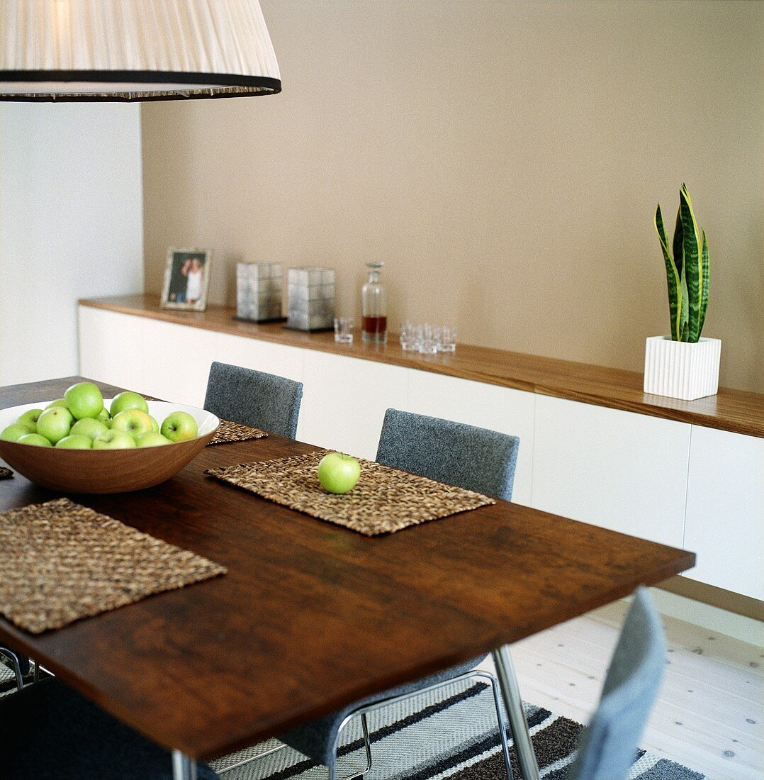 Eine Schale mit grünen Äpfeln auf einem Esstisch mit Holzplatte