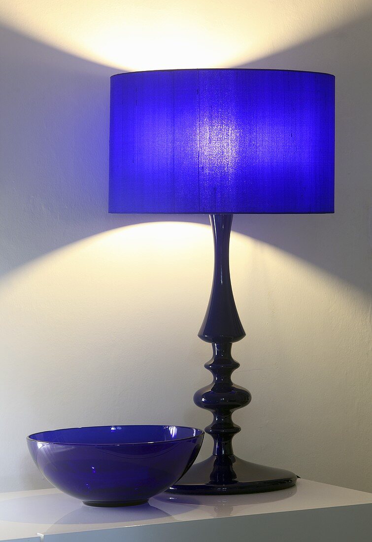 A table lamp with a blue shade next to a blue glass bowl