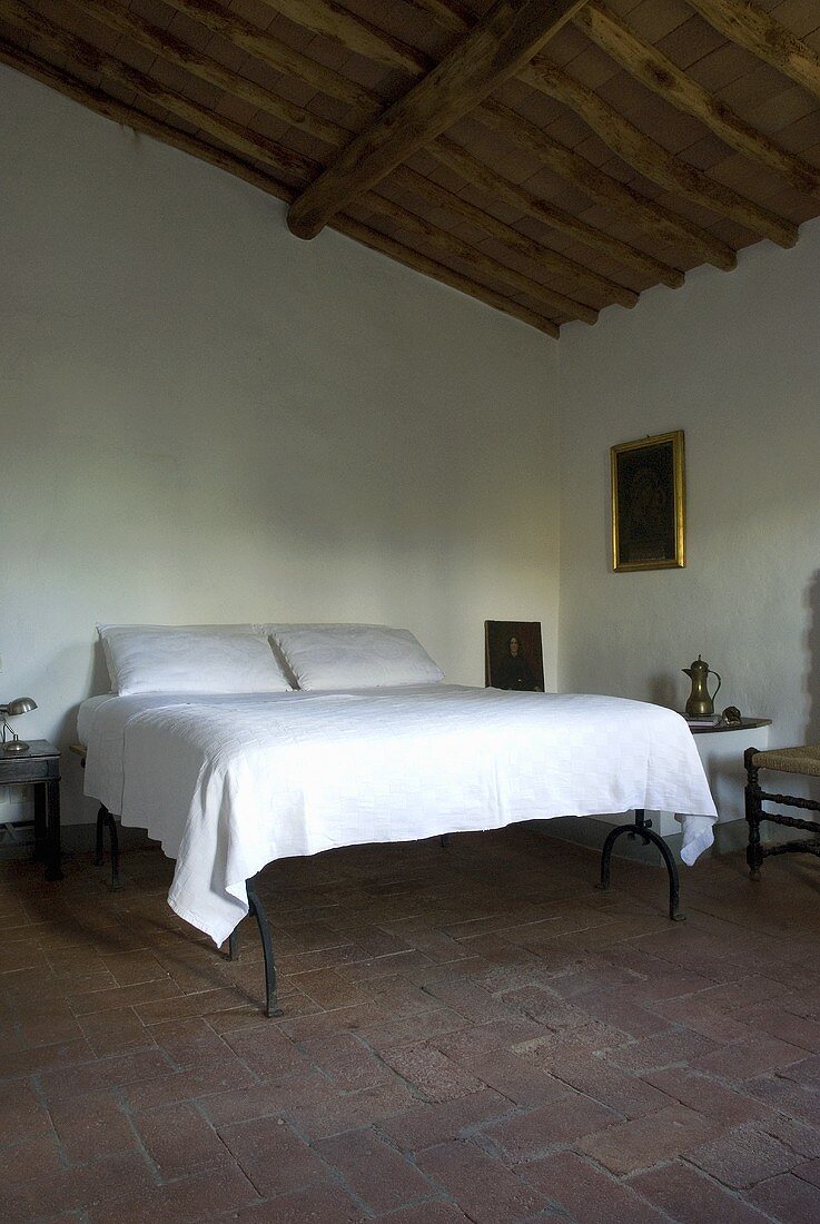 Ein erhöhtes Doppelbett mit weisser Bettwäsche in einem Schlafzimmer mit Terrakottaboden und Holzbalkendecke
