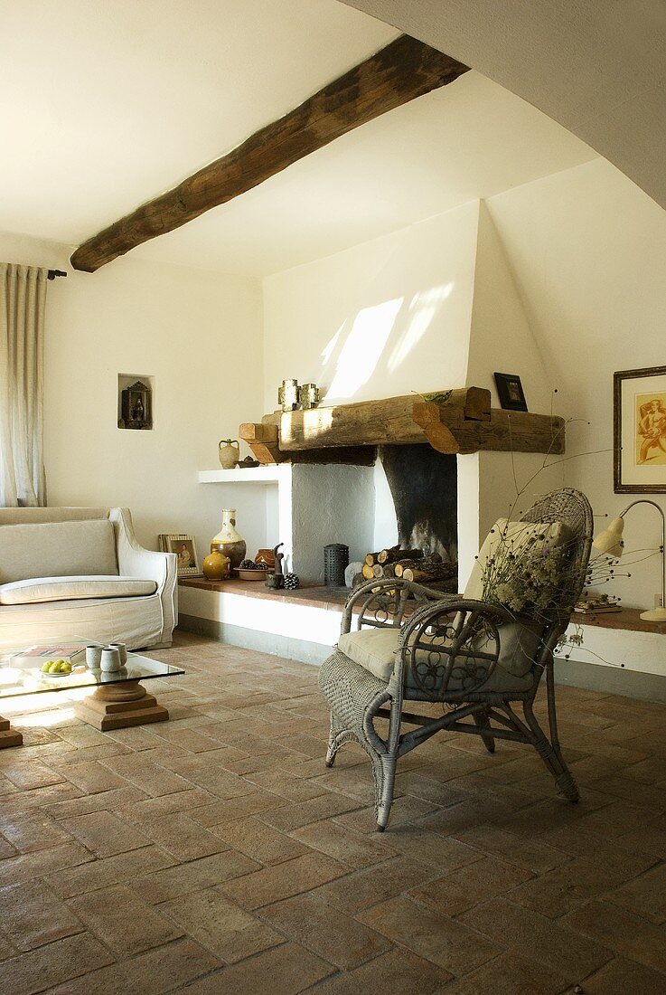 A old rattan chair in front of a fireplace in a living room with a terracotta floor