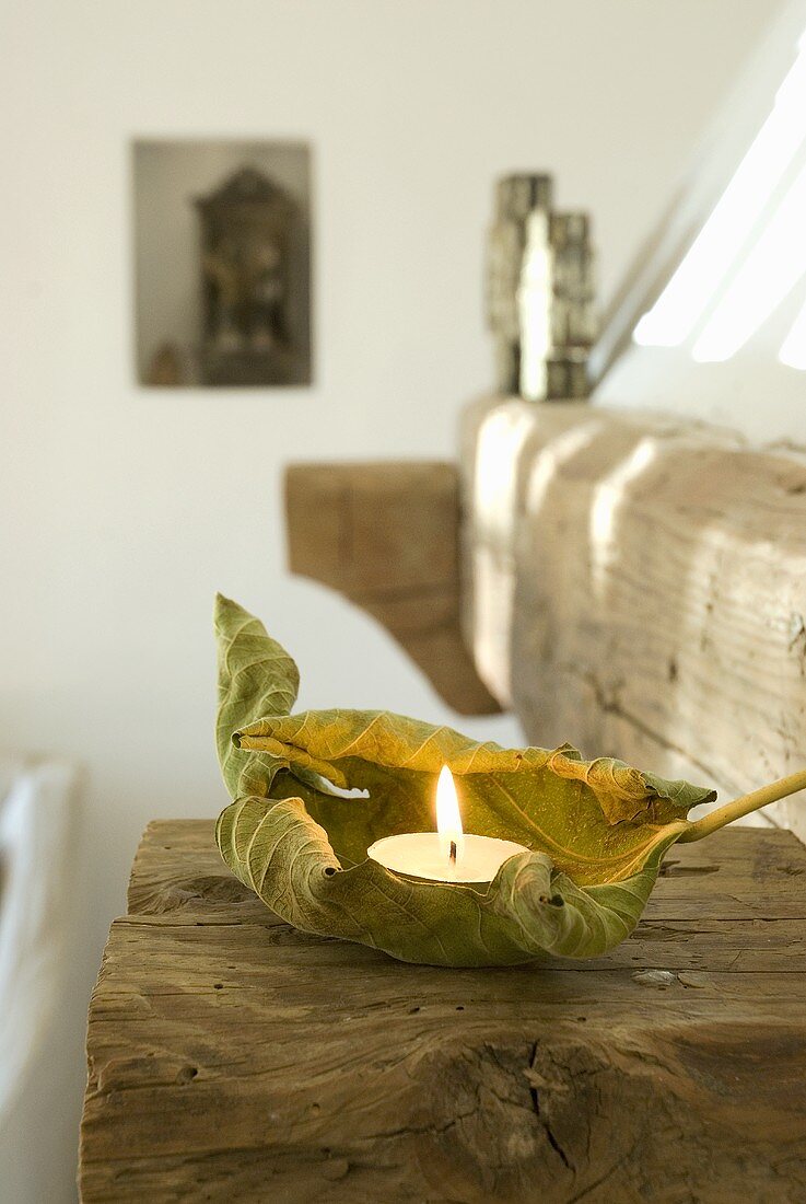Ein getrocknetes Blatt mit Teelicht auf einem Holzbalken