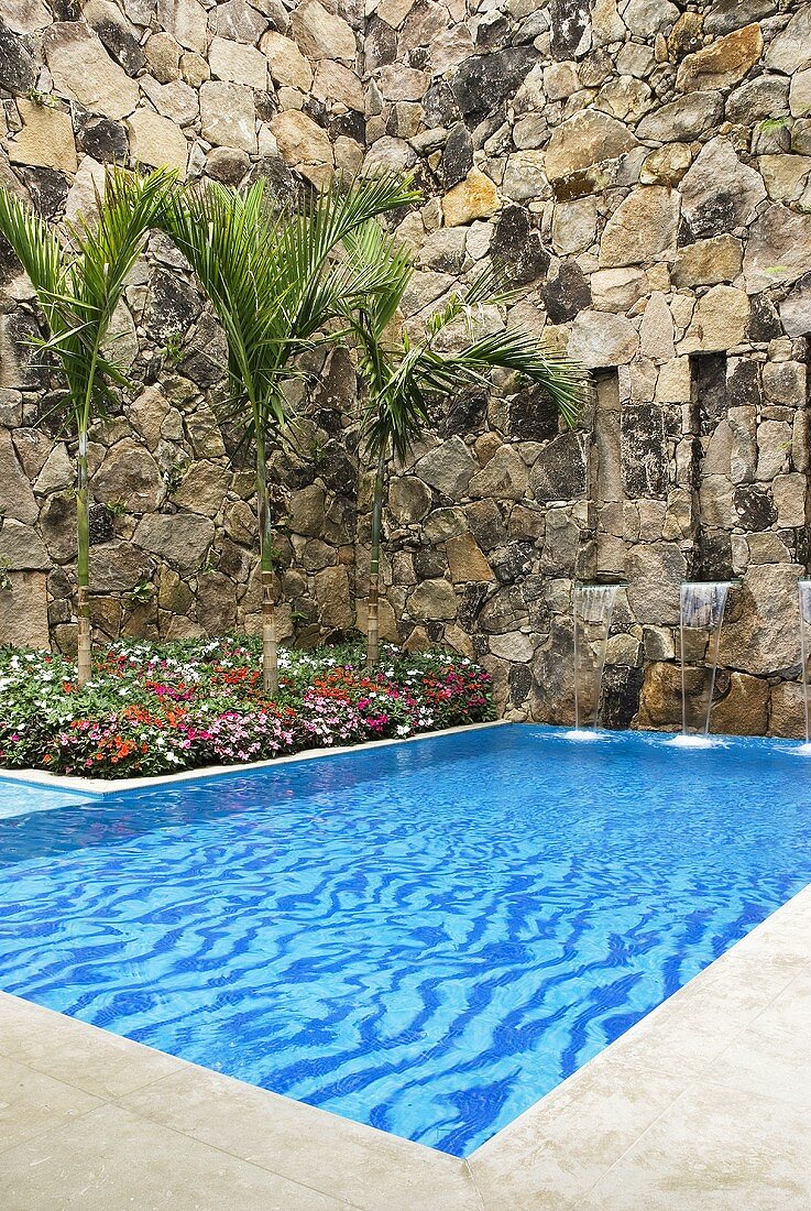 Ein Pool mit kleinen Wassserfällen, umgeben von einer Natursteinmauer