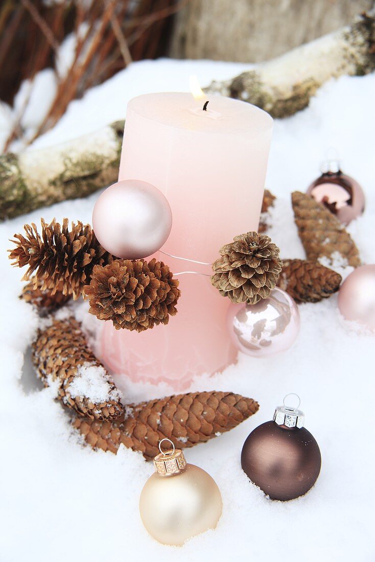 Rosa Kerze mit Zapfen und Weihnachtskugeln im Schnee