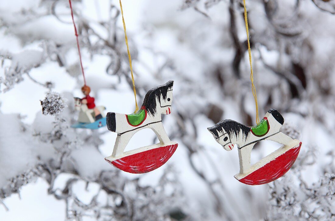Kleine Schaukelpferde aus Holz hängen an einem verschneiten Baum