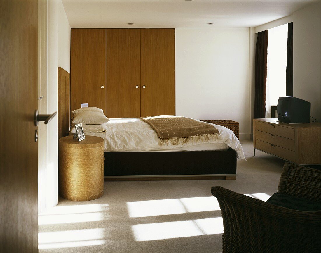 Blick durch offene Tür in modernen Schlafraum auf Doppelbett und Einbauschrank mit Holzfront