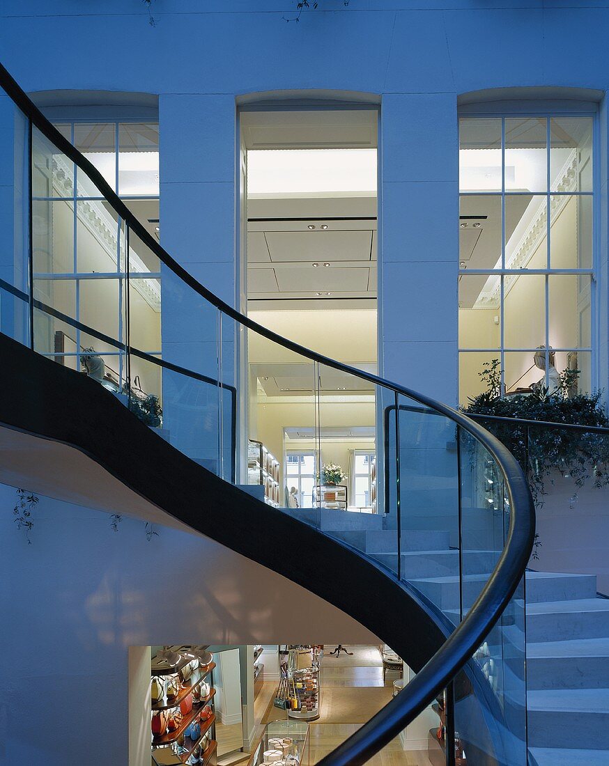 Curved exterior staircase in the twilight and a view into an illuminated loft like apartment