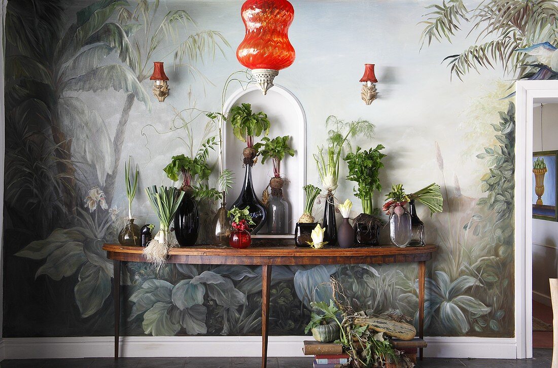 Verschiedenes Gemüse in Glasvasen auf einer Konsole vor einer bemalten Wand