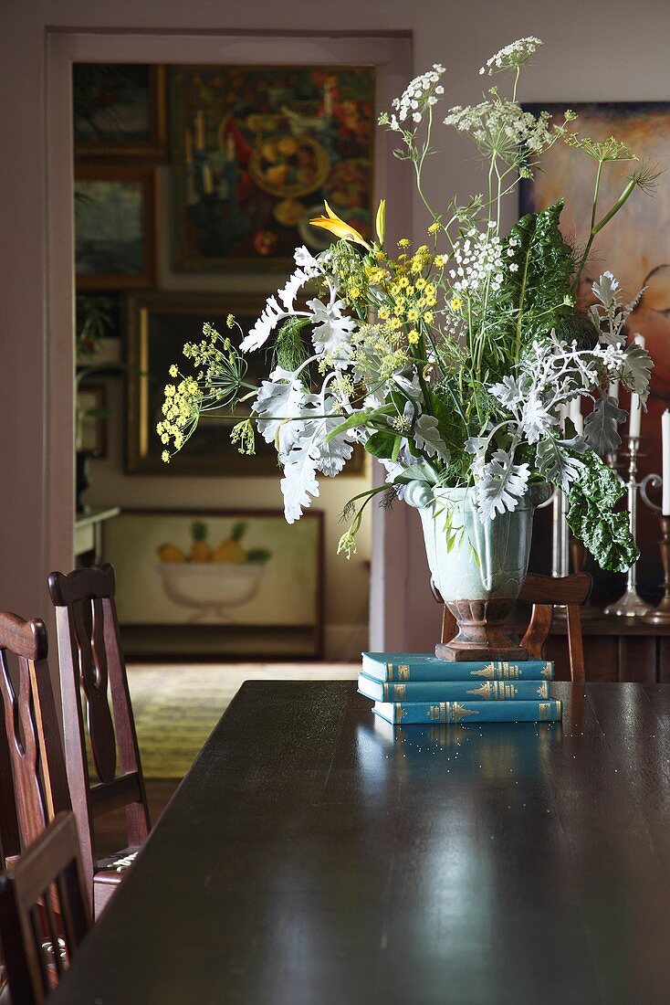 Vase with herbs on a stack of books on a dining table