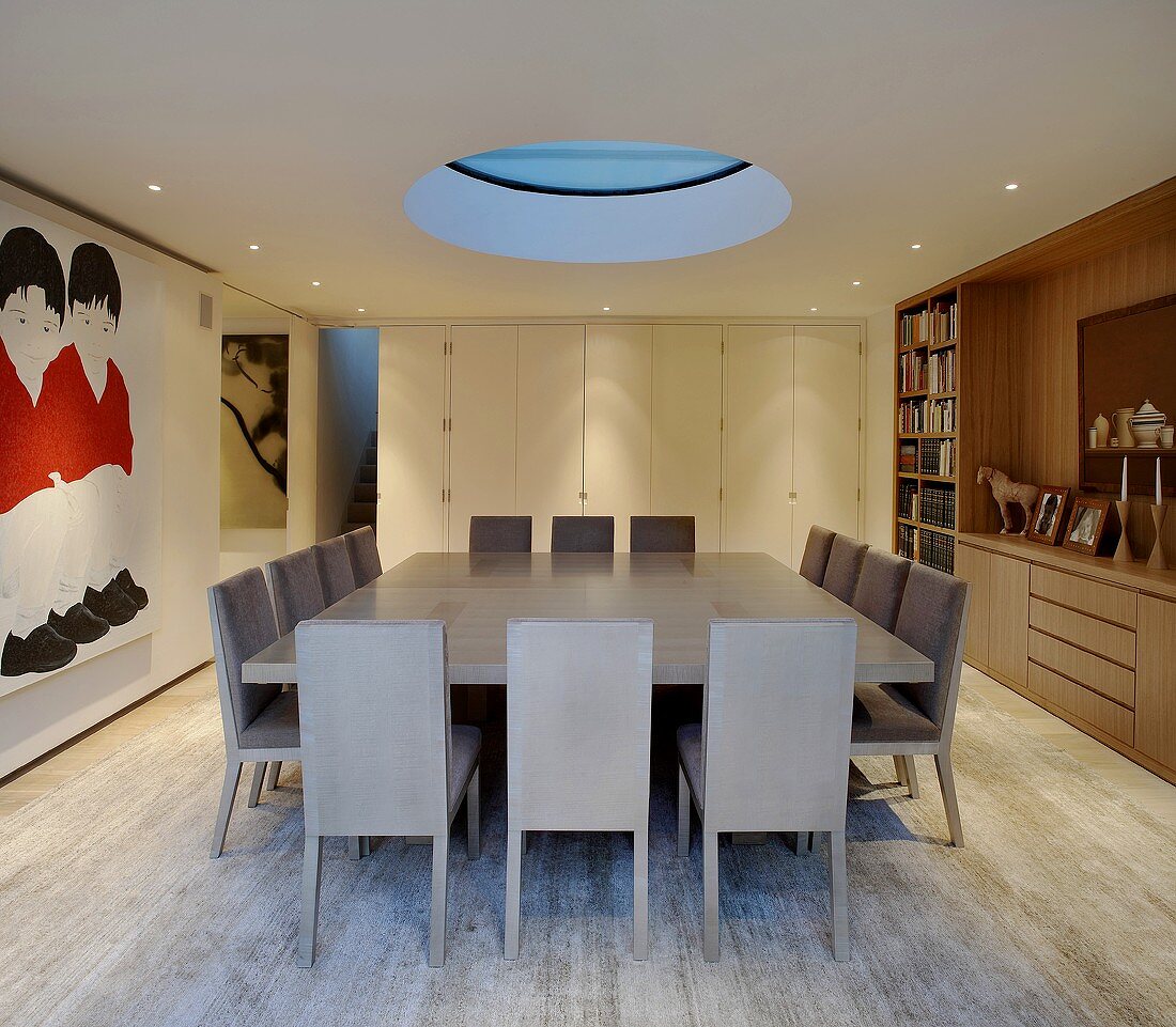 Grosser Esstisch mit Stühlen in Grau unter kreisförmigem Oberlicht im modernen Esszimmer