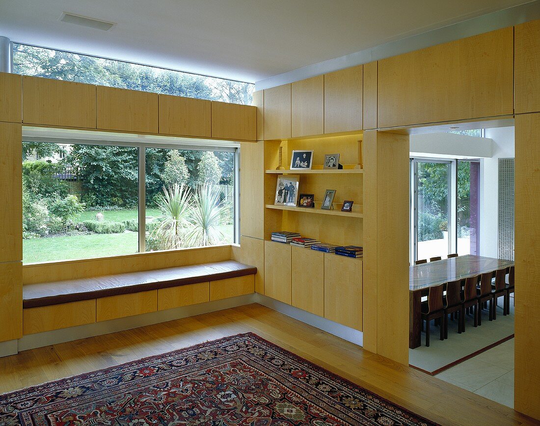 Corner of a room with tailor-made, built in wooden furniture in front of a window with an oriental rug on the floor