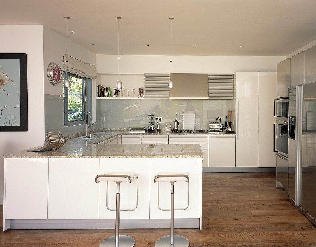 Open white designer kitchen with chrome swivel bar stools in front of a counter