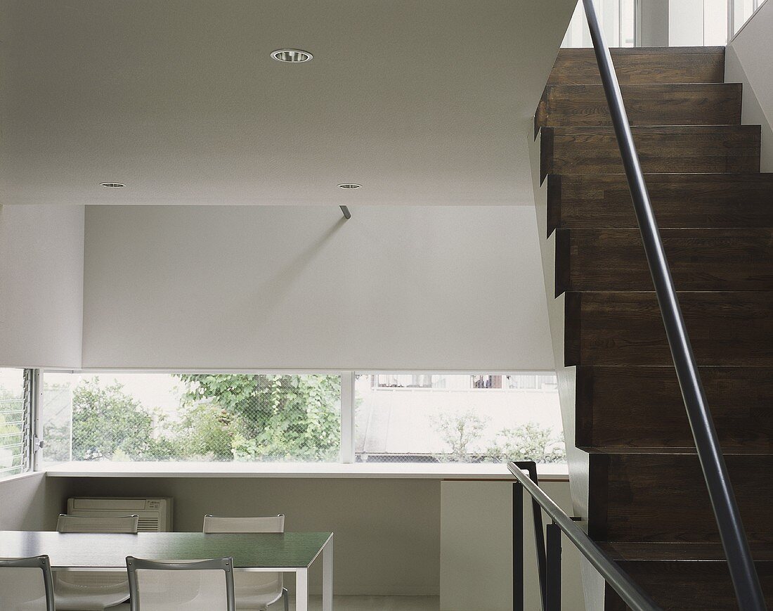 Minimalistischer Wohnraum mit Treppe aus dunklen Holzstufen und Tisch mit Stuhl vor Fenster