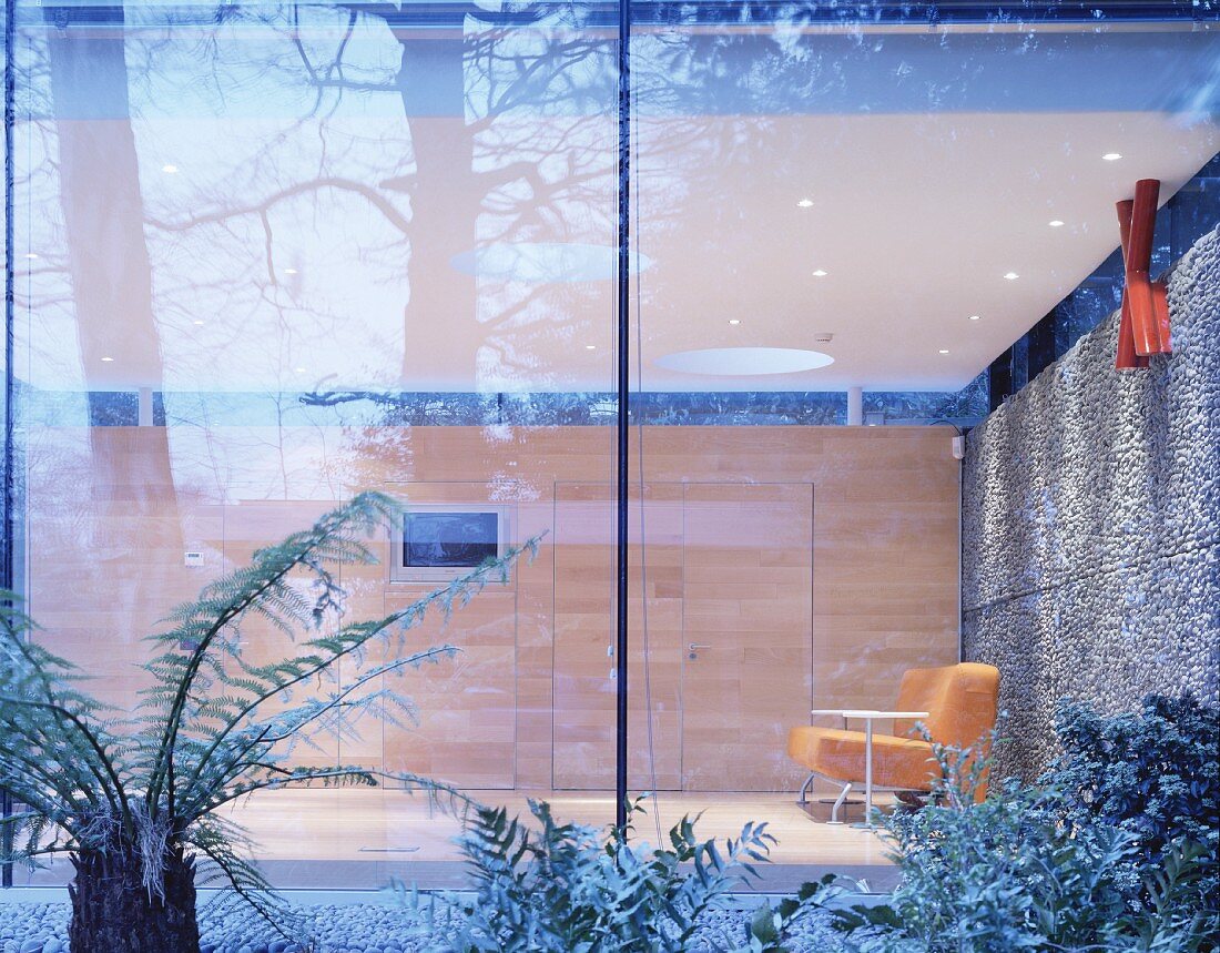 Garten vor Glasfassade und Blick in minimalistischen Wohnraum auf Sessel