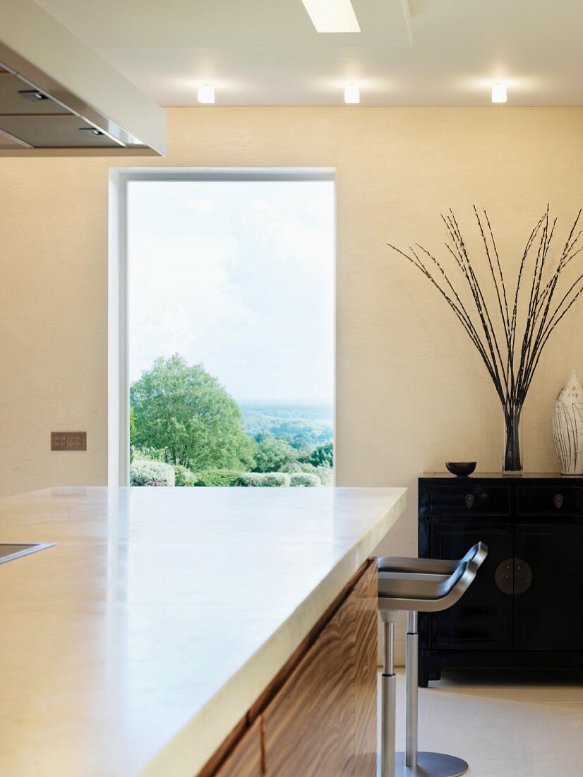 Küchenblock mit weisser Arbeitsplatte vor Fenster mit Landschaftsblick in Designerküche