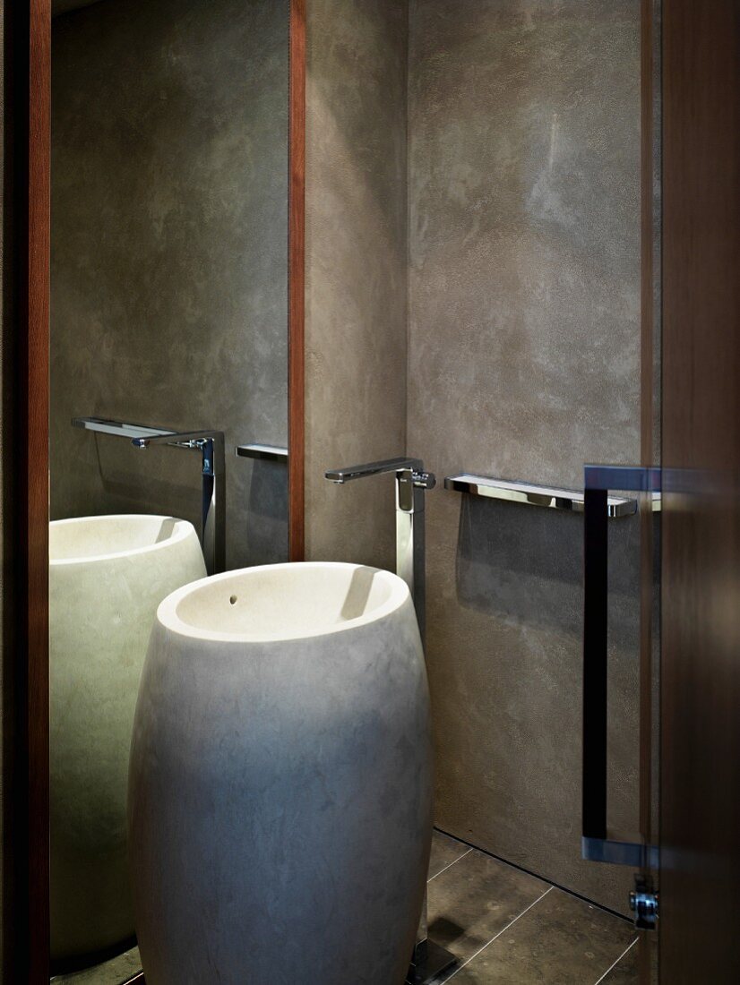 Artistic designer bath with barrel-like standing stone wash basin in front of a mirror and grey wall in faux finish