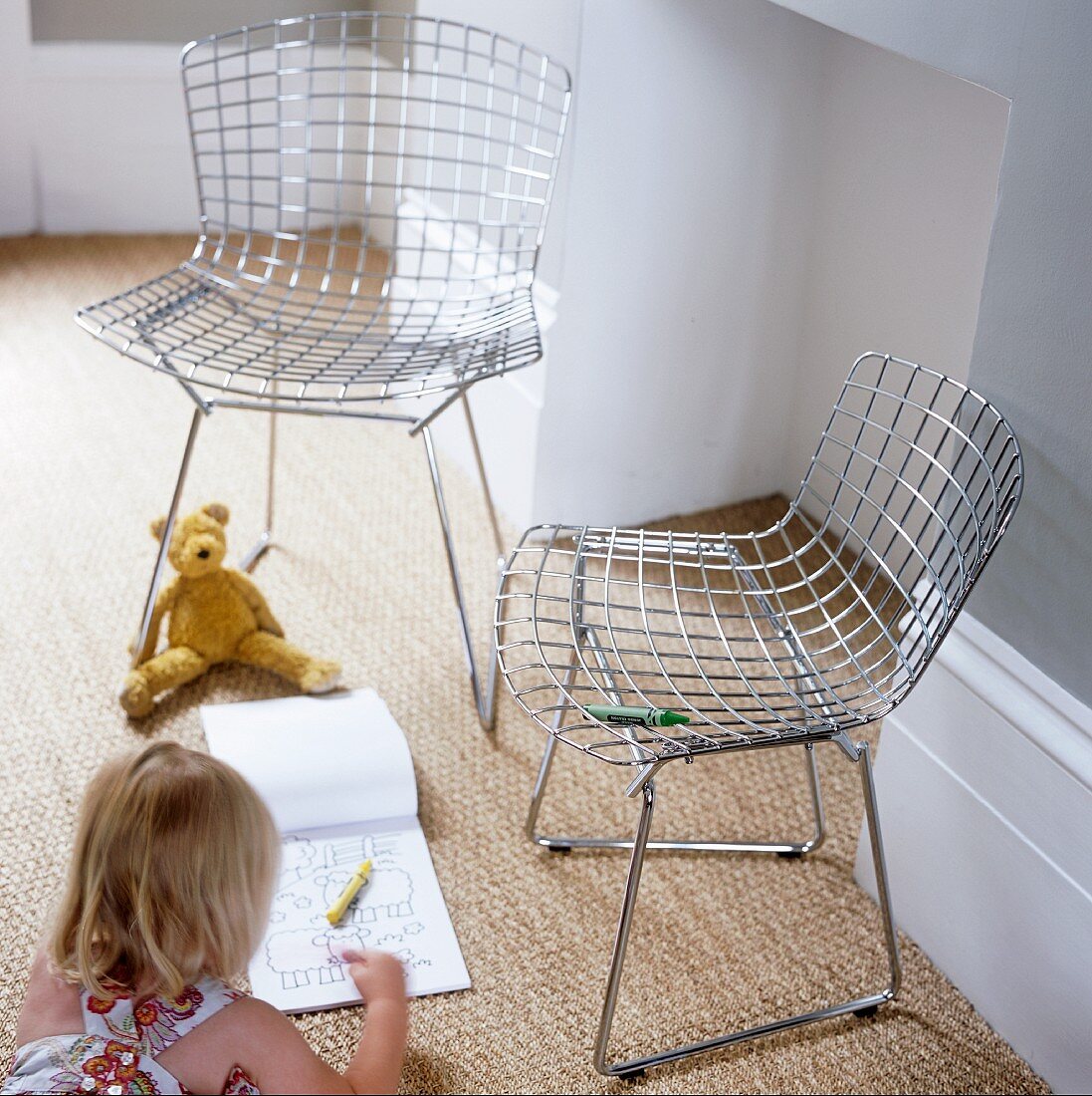 A pair wire mesh chairs and little girl drawing on the carpet
