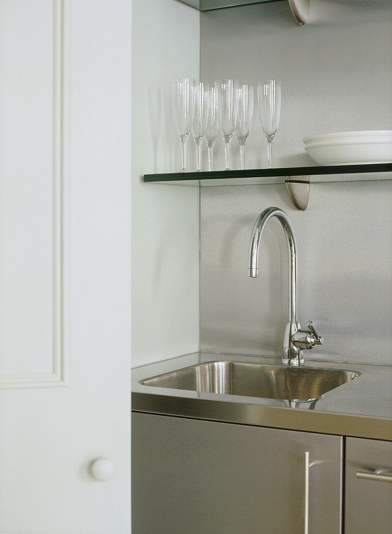 A detail of a modern kitchen, stainless steel sink unit, shelving, glassware
