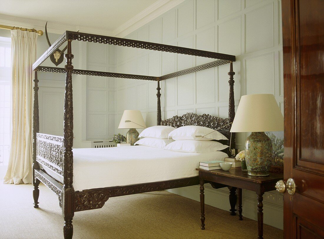 Traditionelles Schlafzimmer mit holzgeschnitztem Himmelbett und Lampen auf Nachttisch