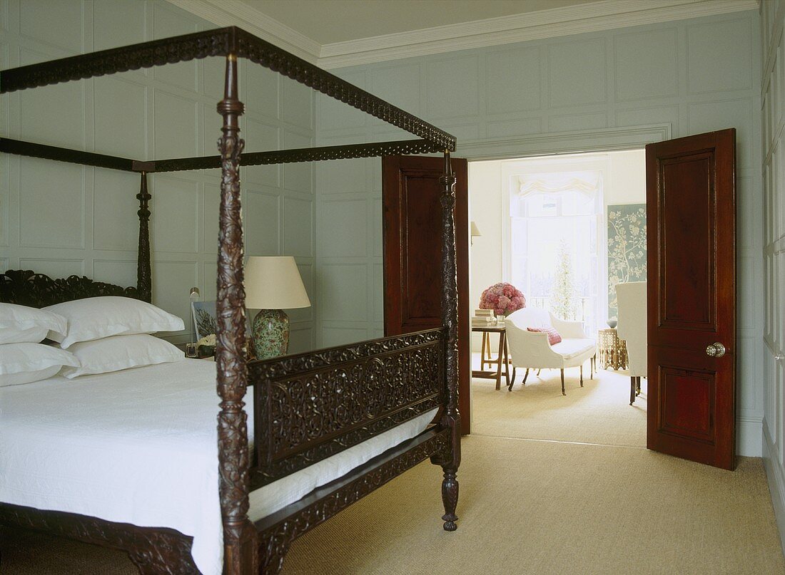 Traditionelles Schlafzimmer mit holzgeschnitztem Himmelbett und offene Flügeltür mit Blick ins Wohnzimmer