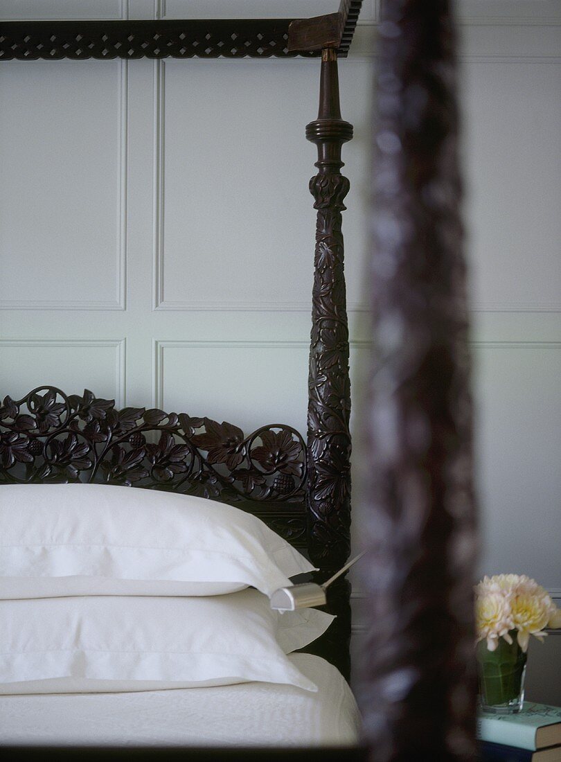 A detail of a traditional bedroom with painted panelling, carved wooden four poster bed
