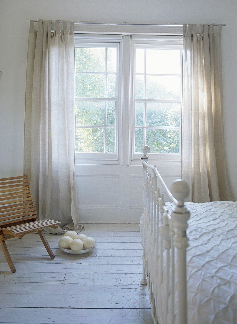White room with Victorian frame bed and wooden chair and ostrich eggs in window.