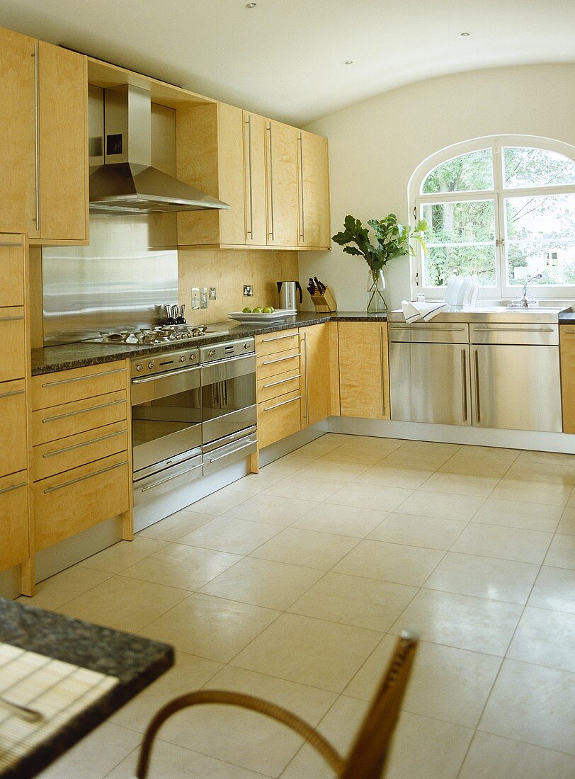 A modern, neutral kitchen with dining area, tiled floor, wood units, stainless steel sink unit, range oven
