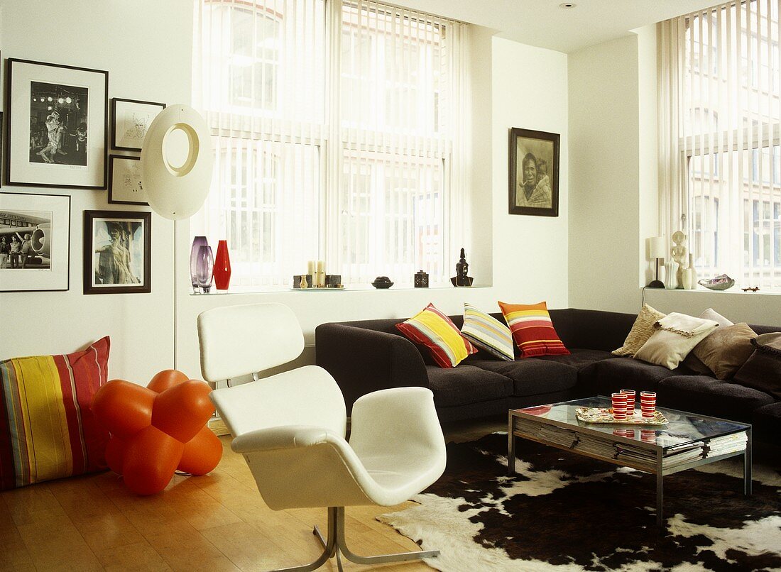 Eclectic sitting room with a wood floor, black sectional sofa, modern armchair, colourful cushions, and an animal skin rug.